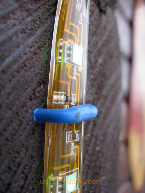 Rubber coated wire staple securing waterproof IP68 24V RGB Flexible LED Strip to the side of a log cabin house.
