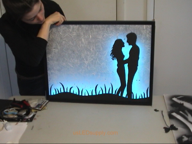 Attach RGB flexible LED strips to the bottom edge of the poster frame and on the glass behind the couple.