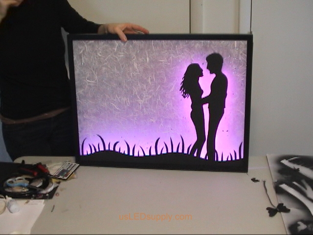 Attach RGB flexible LED strips to the bottom edge of the poster frame and on the glass behind the couple.
