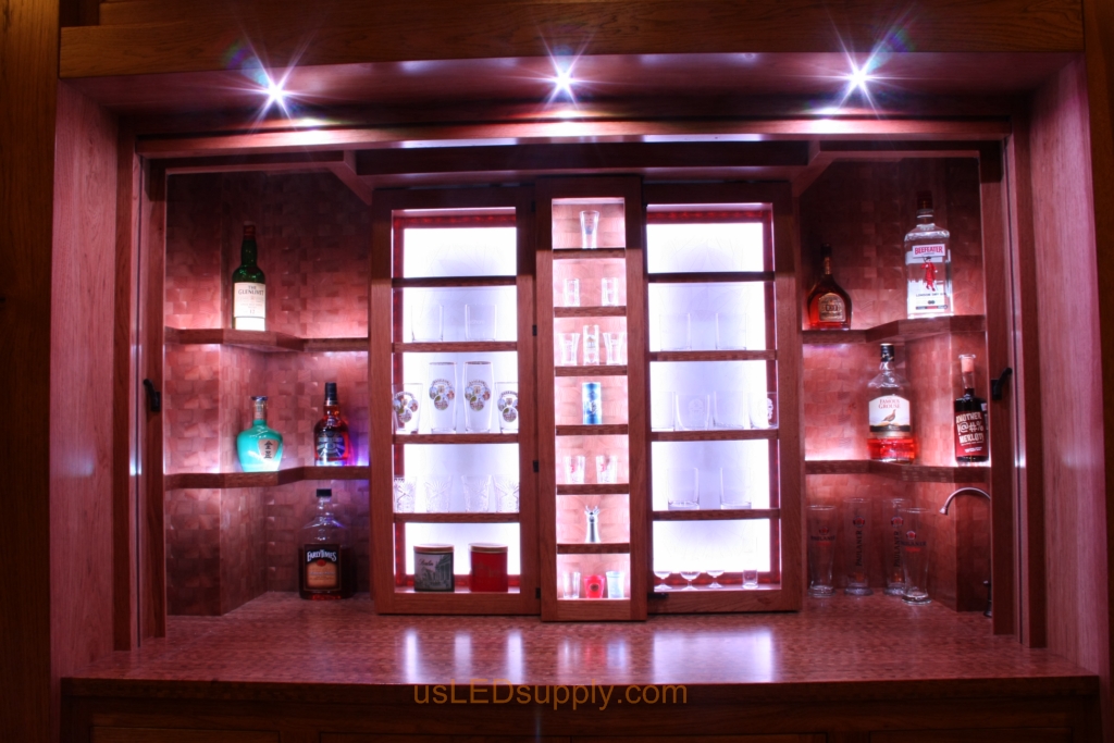 The cabinets open up to reveal the bar with shelves holding liquer bottles and glasses.